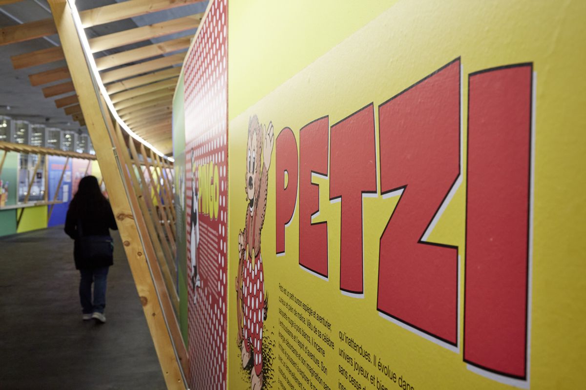 Vue intérieure d’une exposition avec un panneau jaune affichant le nom ’Petzi’ en rouge et une illustration.
