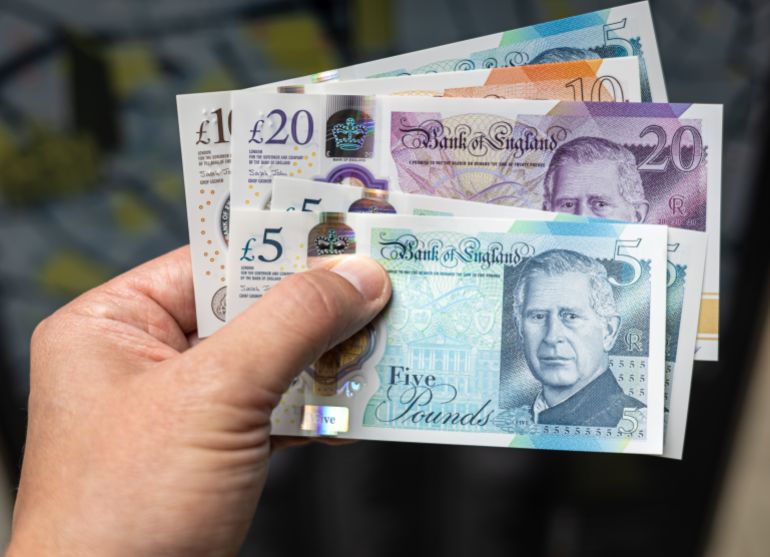 Gros plan sur une main tenant des billets de livre sterling avec le roi Charles III