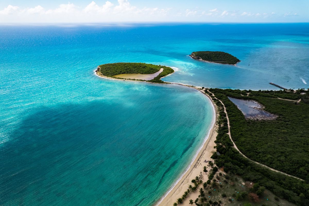 Vue aérienne d’une mer turquoise avec deux petites îles verdoyantes et une plage de sable