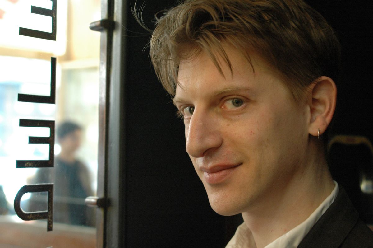 Photo de Jonathan Littell, auteur juif de New York, prise en juin 2006, souriant près d’une fenêtre avec des caractères hébreux sur la vitre.
