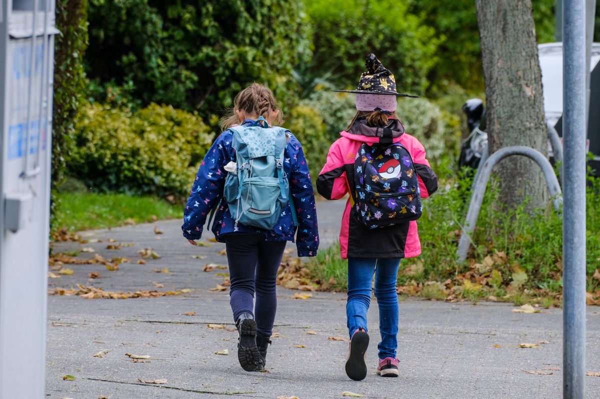 Deux enfants avec des sacs à dos marchant sur un trottoir