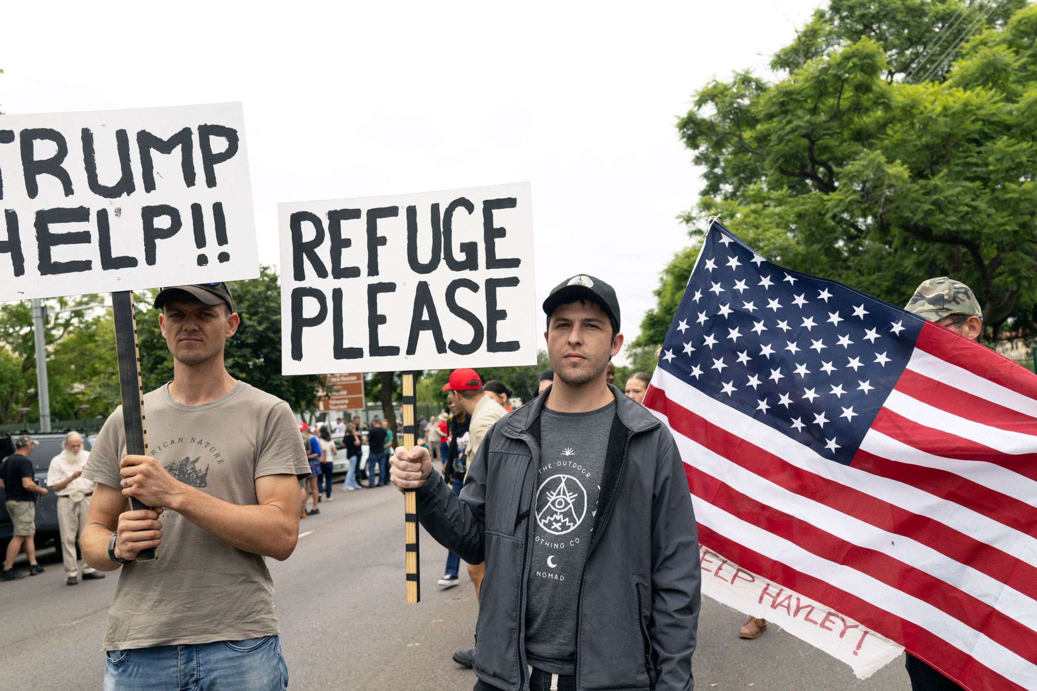 Agriculteurs Afrikaners manifestant devant l'ambassade américaine à Pretoria, Afrique du Sud, le 15 février 2025, tenant des pancartes demandant de l'aide à Trump et un statut de réfugié.