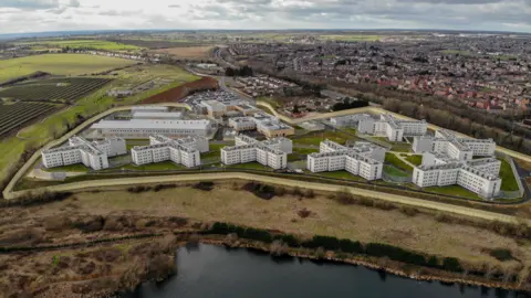 Vue aérienne de la prison HMP Five Wells avec ses sept bâtiments en forme de croix et la ville de Wellingborough en arrière-plan
