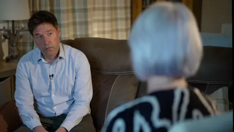 Maria, mère d'un détenu, s'entretenant avec un journaliste, vue floue de dos
