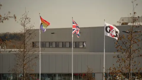 Trois drapeaux flottant devant HMP Five Wells : LGBTQ+, Union Jack et logo G4S