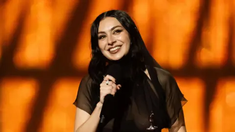 Charli XCX souriant avec un micro