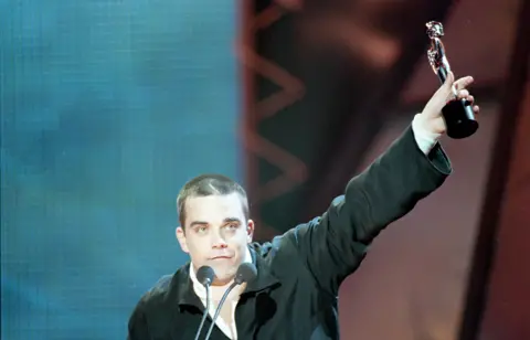 Robbie Williams tenant un trophée Brit Award