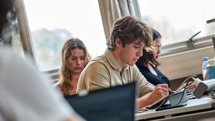 Étudiants concentrés sur leur travail à des bureaux, utilisant des ordinateurs portables et des tablettes dans une pièce bien éclairée