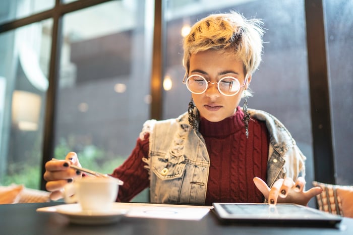 Person sitting in coffee shop looking at tablet.