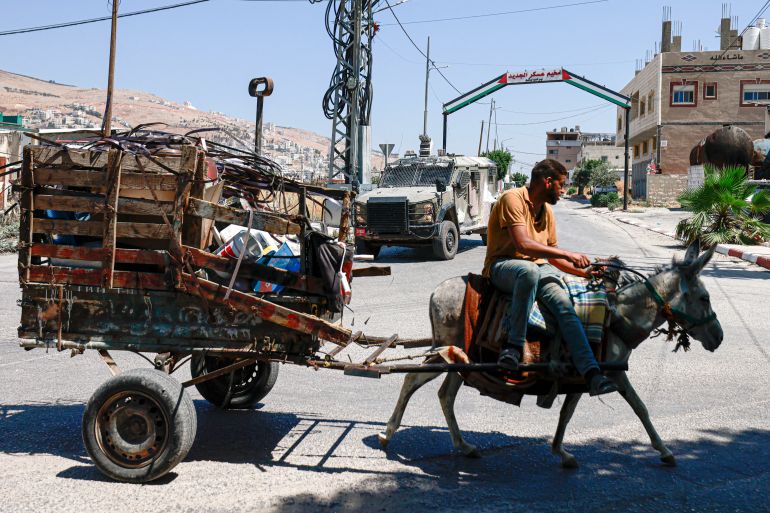 Un homme palestinien conduit sa charrette tirée par un âne devant un véhicule militaire israélien lors d’un raid au camp de réfugiés d’Askar, en Cisjordanie occupée, le 16 juin 2025.