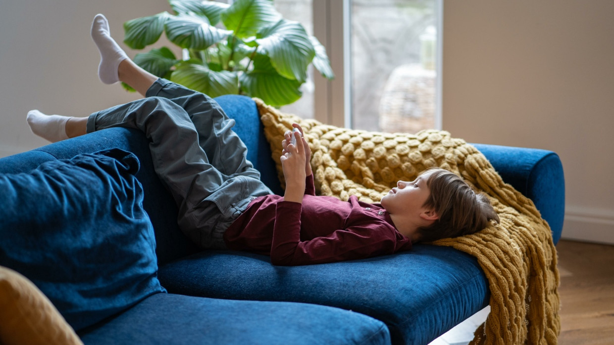 Un enfant avec un smartphone sur le divan. (Image symbolique)