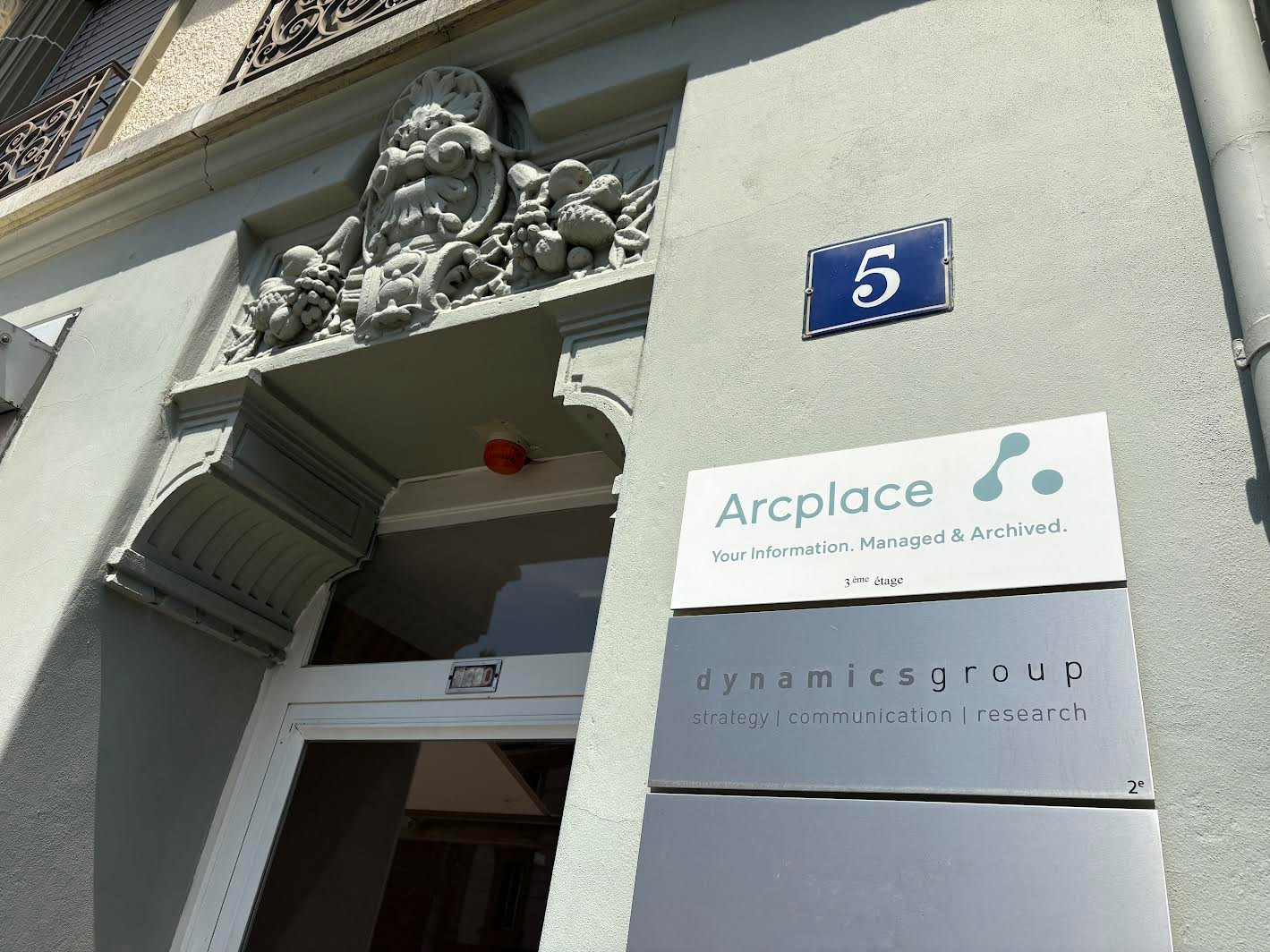 Entrée d’un bâtiment avec les enseignes d’Arcplace et Dynamics Group affichées à côté de la porte.