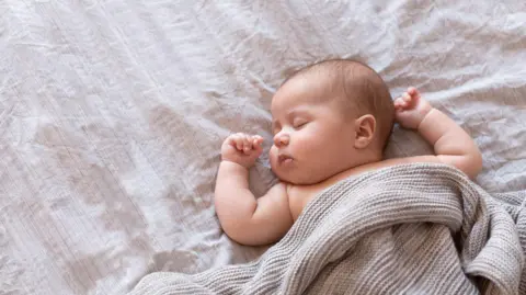 Un bébé repose les yeux fermés sous une couverture