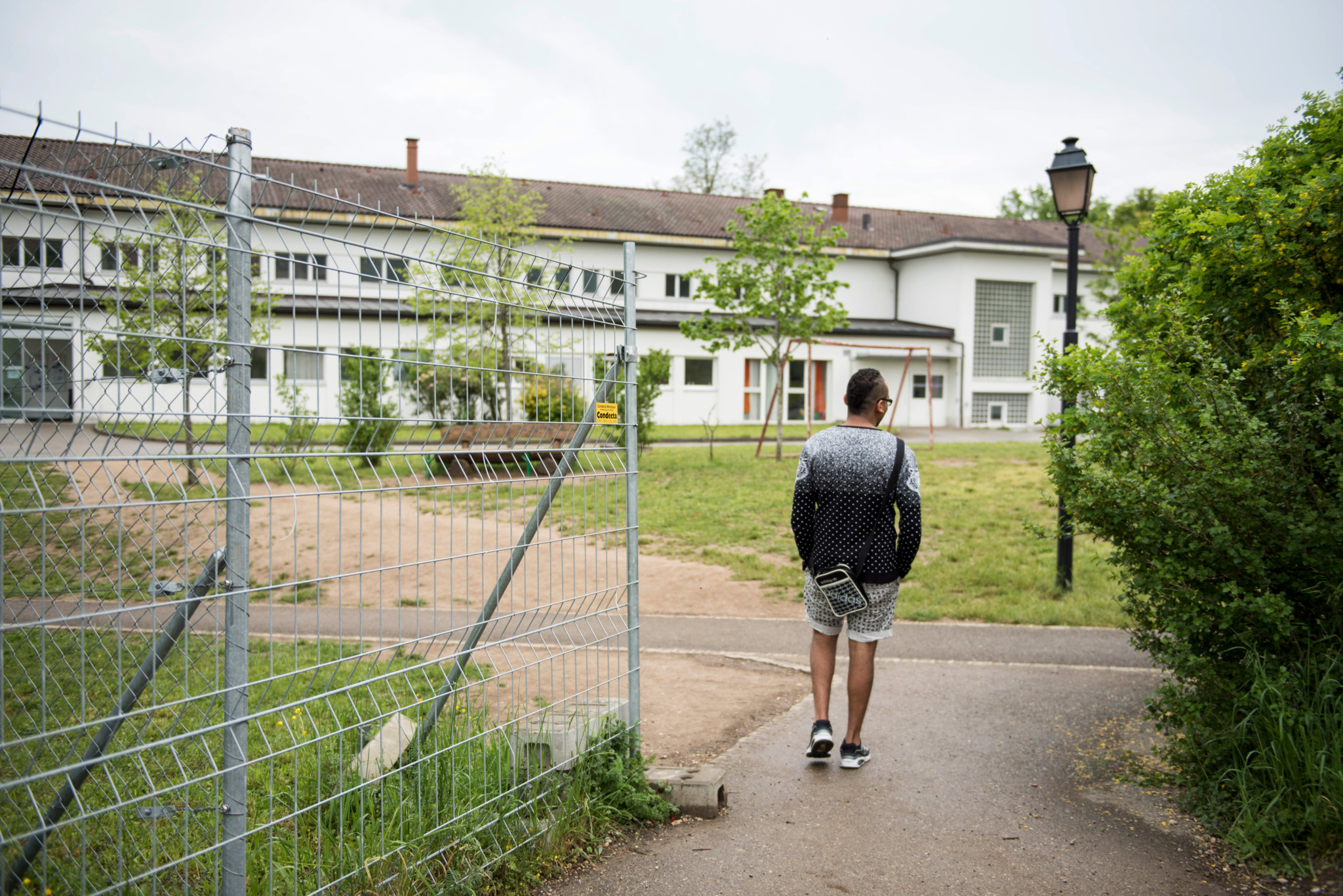 Une personne entre dans le centre fédéral pour demandeurs d’asile Perreux à Boudry, Neuchâtel, vue d’un portail métallique.