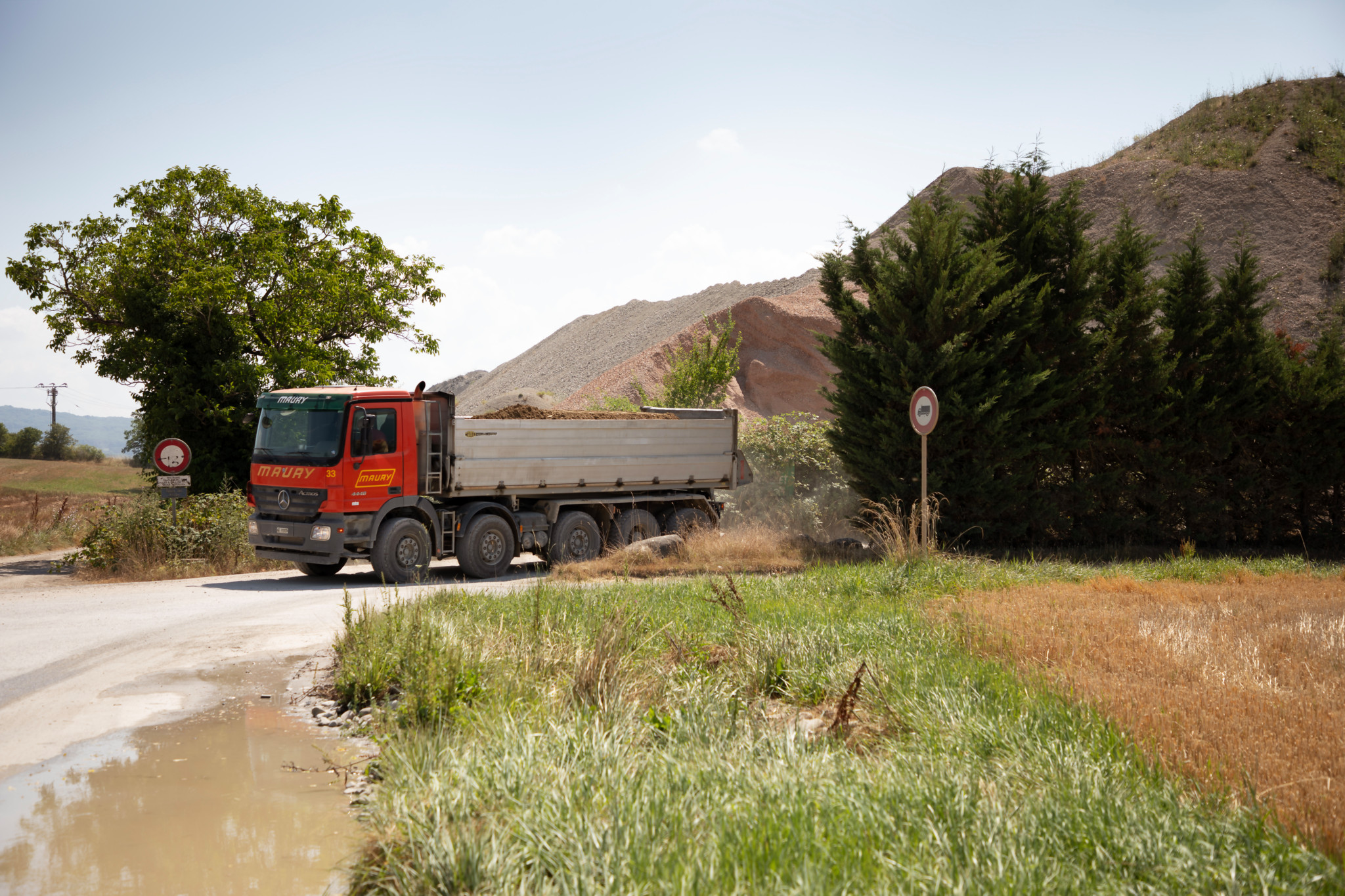 Camion de chantier sur le chemin des Epinglis à Bardonnex, près de la sablière du Cannelet, avec monticules de terre en arrière-plan.