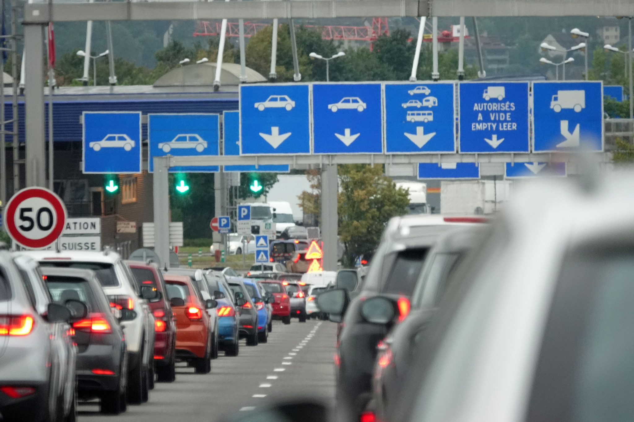 Embouteillage devant la douane franco-suisse de Bardonnex, avec des voitures alignées sous des panneaux de direction.