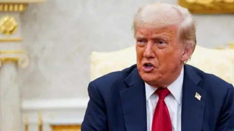 Donald Trump dans le Bureau ovale, vêtu d'un costume bleu marine et d'une cravate rouge.
