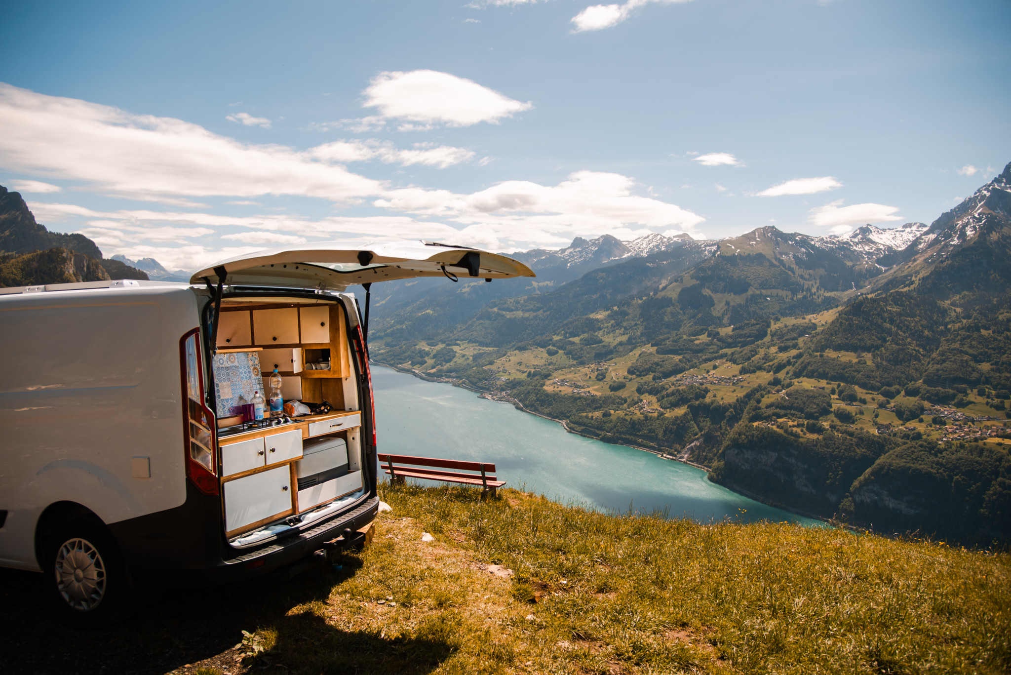 Un van aménagé surplombant le lac Walensee en Suisse, entouré de montagnes verdoyantes sous un ciel ensoleillé.