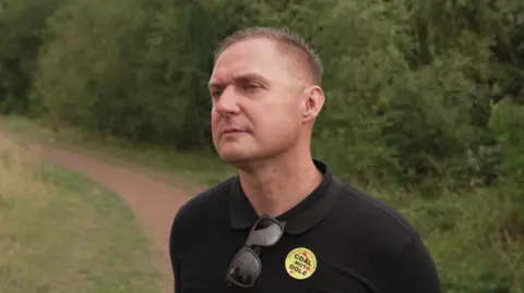 Un homme sur un chemin rural avec un t-shirt affichant un message de solidarité avec les mineurs.