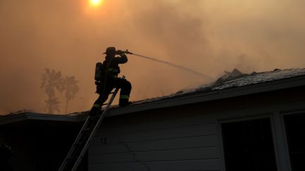 Un pompier arrose la toiture d'une maison en feu à Altadena (Californie, Etats-Unis), le 9 janvier 2025. (JUSTIN SULLIVAN / GETTY IMAGES NORTH AMERICA / AFP)