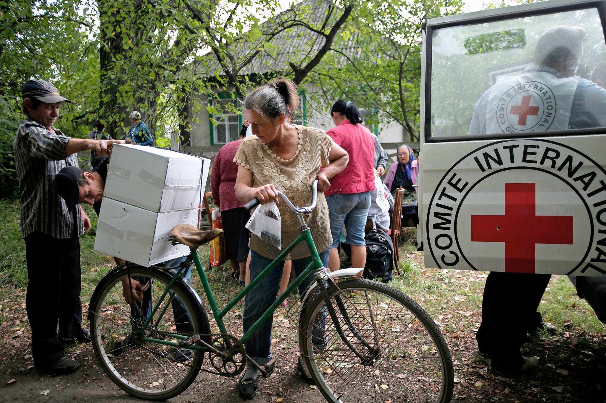 Distribution de nourriture par le CICR aux habitants du village de Novozvanivka, Louhansk, avec résidents portant des cartons et un véhicule du CICR en arrière-plan.