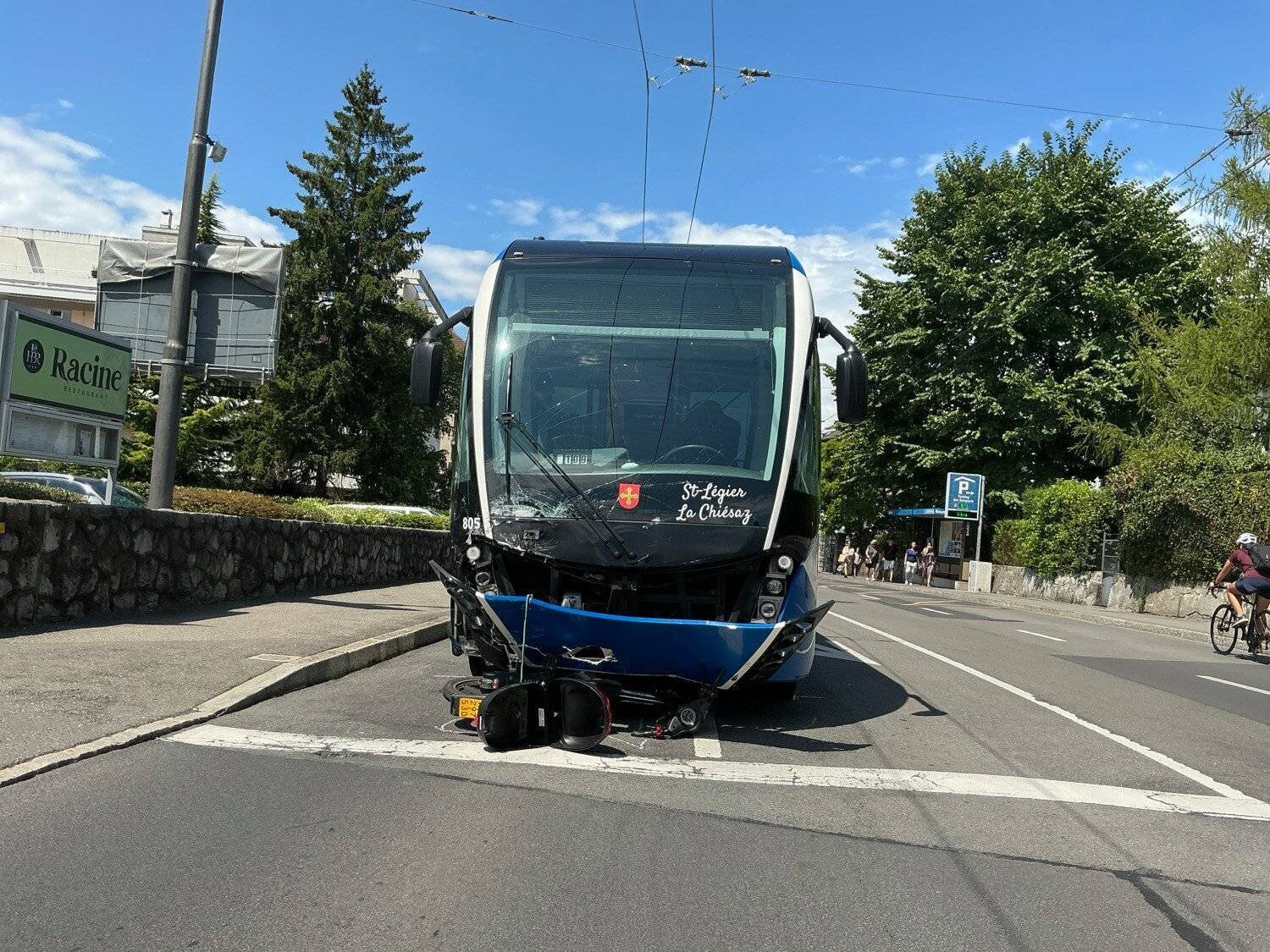 Un tramway St-François – Le Châlet à l’arrêt après une collision, avec des dommages visibles à l’avant, sur une route ensoleillée bordée d’arbres.