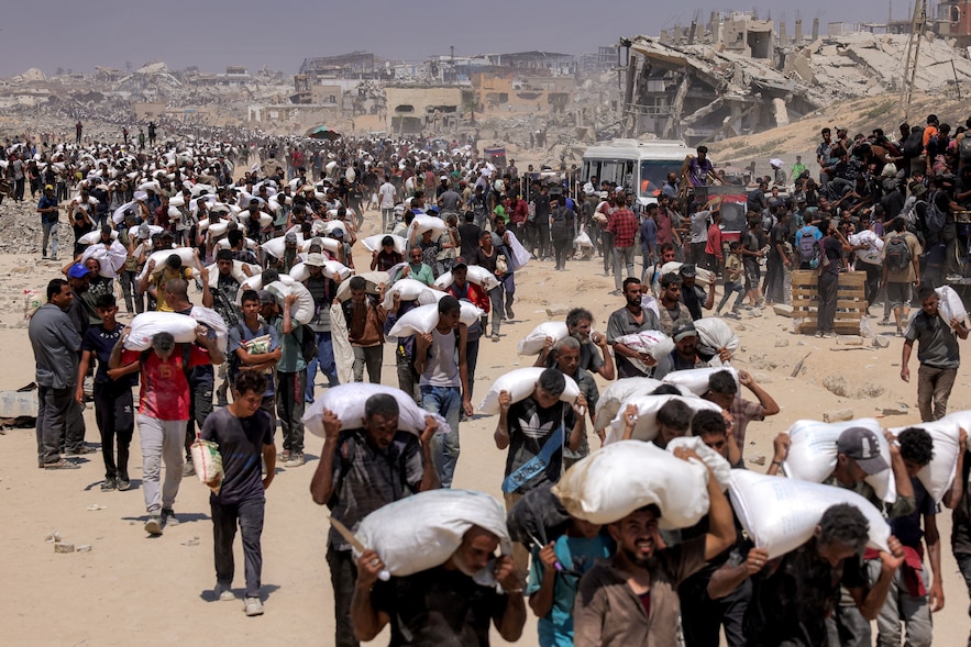 Des habitants de Gaza portent des sacs de farine qu'ils ont reçus après l'entrée de camions d'aide humanitaire par le point de passage de Zikim, dans le nord du territoire, le 27 juillet 2025