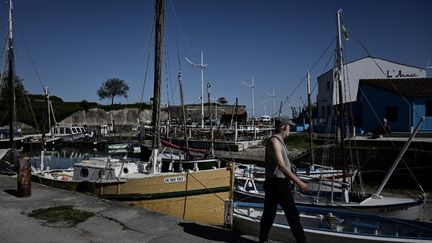 Un homme passe devant des bateaux amarrés dans le port du Château-d'Oléron sur l'île d'Oléron (Charente-Maritime), le 8 avril 2025. (PHILIPPE LOPEZ / AFP)