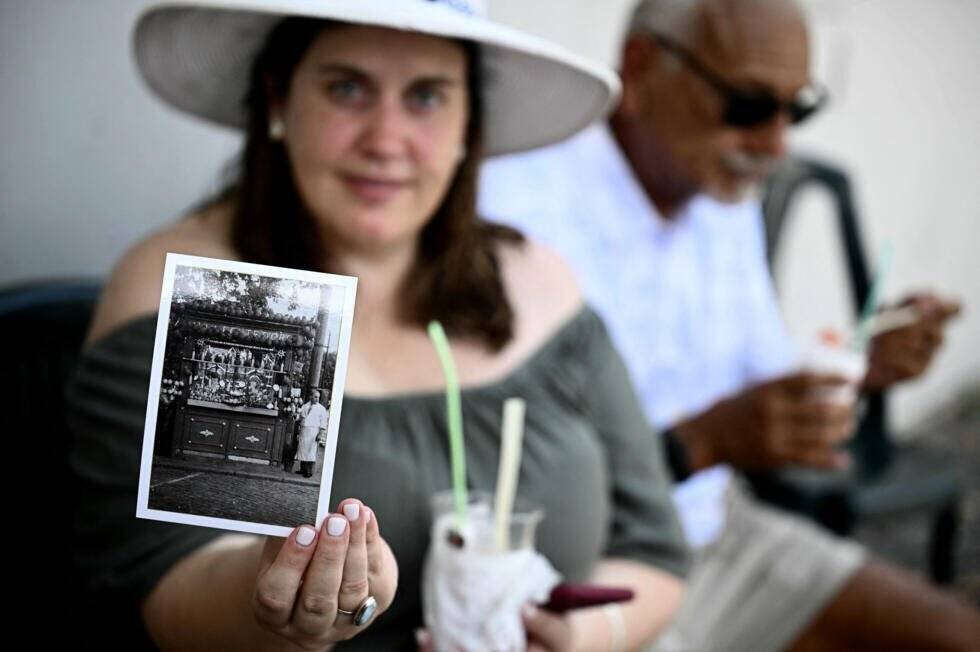 Une femme tient une vieille photo représentant un kiosque et mange une « Grattachecca »