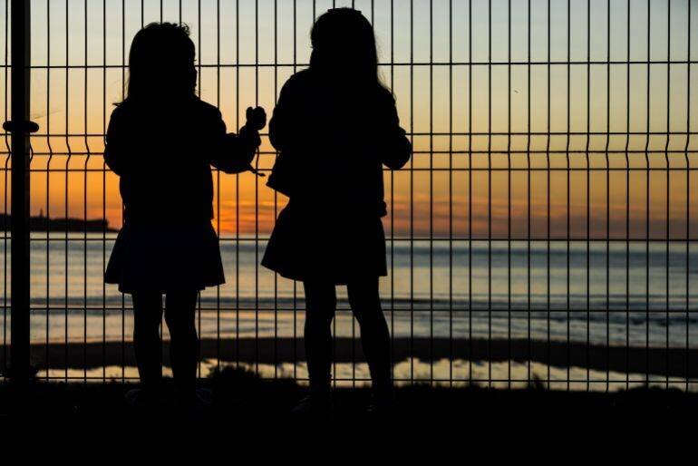 Deux filles grimpant une clôture au coucher du soleil, concept de pauvreté et vulnérabilité