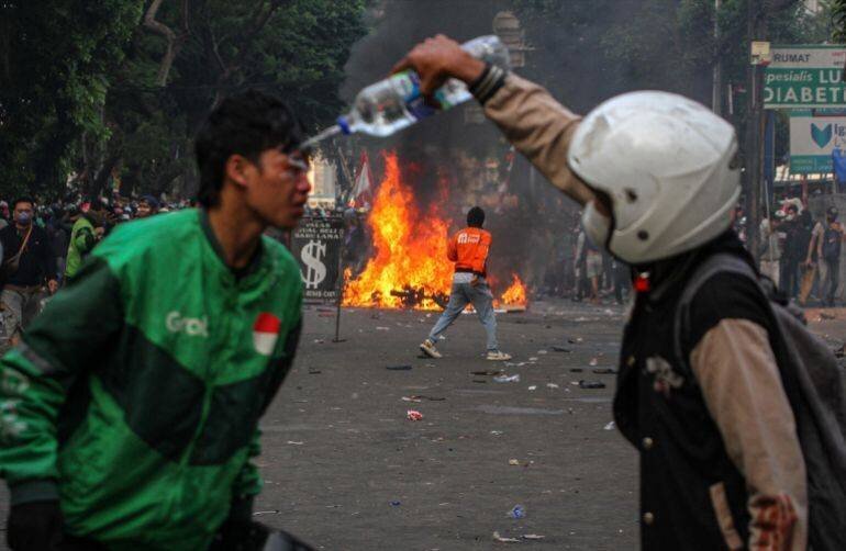 Manifestant aspergeant d'eau les yeux d'un autre manifestant pour neutraliser le gaz lacrymogène lors d'une manifestation à Jakarta