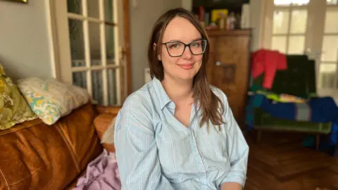 Elissa assise sur un canapé en chemise rayée