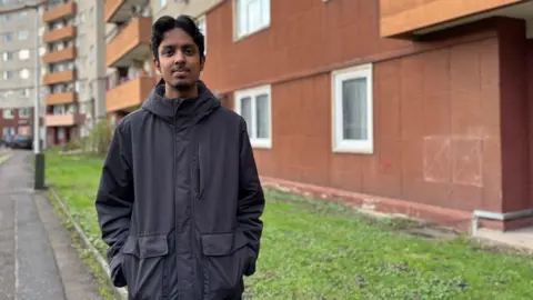 Iftikhar Ali debout devant Westfield Court, regardant la caméra